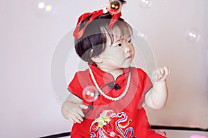 Cute Chinese little baby in red cheongsam play soap bubbles