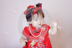 Cute Chinese little baby in red cheongsam play soap bubbles