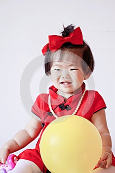 Cute Chinese little baby in red cheongsam play yellow balloon