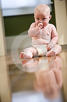 Cute chubby baby wearing diaper sitting on floor photo