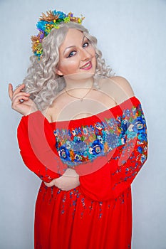 Cute chubby girl with flowers in white curly hair in red rustic dress