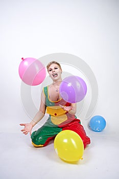 Cute chubby girl with short blonde hair and plus size figure in bright colored PVC jumpsuit posing with air balloons on white back