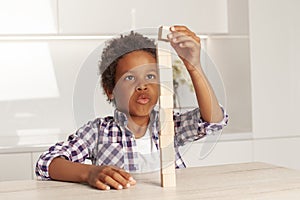 Cute clever child small boy playing and building a tower of wooden blocks at home