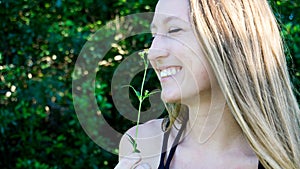 Cute close portrait of a young blonde woman face smiling laughing with closed eyes and a daisy flower isolated in nature