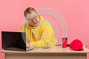 Cute comic man in bright casual wear working on computer with funny face