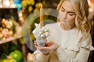 Cute composition in pot of white Christmas balls and golden candle in hands of woman