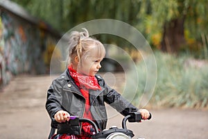 Cute cool child girl in leather jacket riding the motorbike in summer park