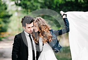 Cute couple embraces. Portrait of stylish young man in suit with tie hugs beautiful girl holding white dress in air. Concept of