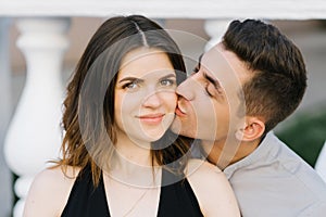 Cute couple in love posing on the street. A young man kisses a happy smiling woman on the cheek