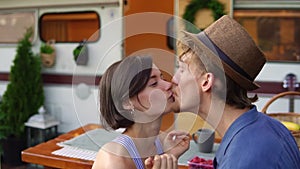 Cute couple man and woman having fun together at wooden table outdoors, girl putting her hat on a man`s head. Man joking