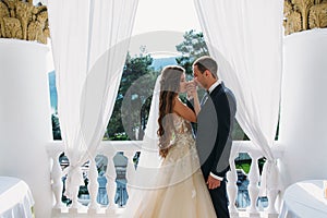 A cute couple of newlyweds kiss each other`s hands. The bride and the bridegroom hold their teeth. The bride in a black