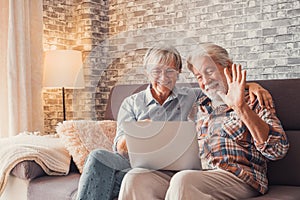 Cute couple of old people sitting on the sofa using laptop together shopping and surfing the net. Two mature people in the living