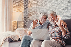 Cute couple of old people sitting on the sofa using laptop together shopping and surfing the net. Two mature people in the living