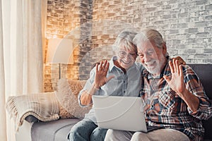 Cute couple of old people sitting on the sofa using laptop together shopping and surfing the net. Two mature people in the living