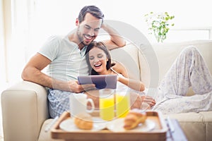 Cute couple relaxing on couch with tablet at breakfast