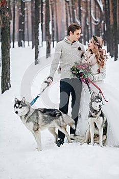 Cute couple with two siberian husky are posed on background of snowy forest. Winter wedding. Artwork