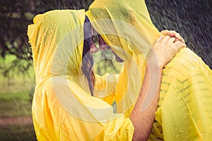 Cute couple wearing protection cape and hugging under the rain