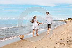Cute couple of young lovers with a dog walk along the beach