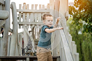 A cute curious toddler boy of two or three years playing on a wooden playground outside. Active games and entertainment for