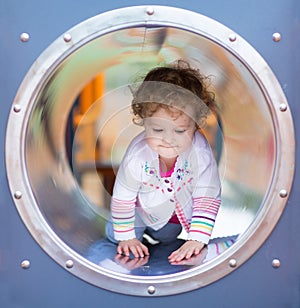 Cute curly baby girl climbing a slide on a playground