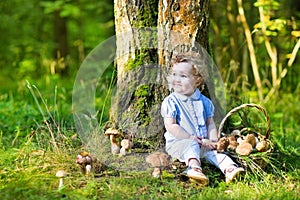 Cute curly baby girl gathering mushrooms in autumn forest