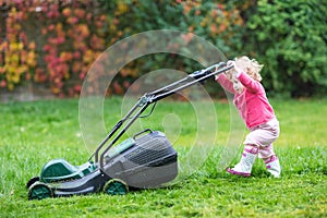 Cute curly baby girl with lawn mower in the garden