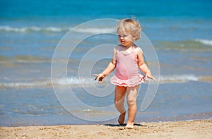 Cute curly baby girl playing on a beautiful tropical beach wearing a cute swimsuit