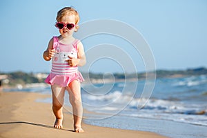 Cute curly baby girl playing on a beautiful tropical beach wearing a cute swimsuit