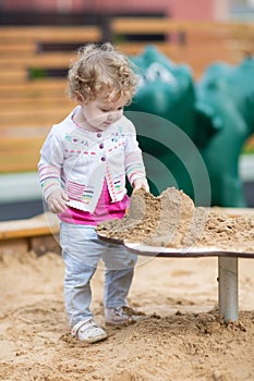 Cute curly baby girl playing with sand on a playground