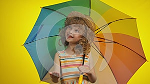 A cute curly blond girl in a straw hat with a rainbow umbrella