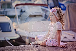 Cute curly blonde child girl in pink skirt sitting in docks