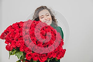 Cute curly brunette girl standing, smelling red roses over white background.