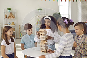 Cute curly dark-skinned girl carefully pulls out a brick while her friends watch and cheer.