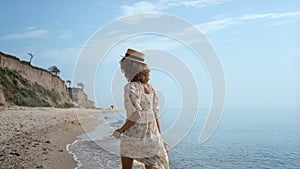 Cute curly girl dancing on ocean waves holding dress. Smiling woman have fun.