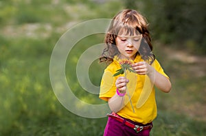 Cute curly girl in a yellow t-shirt on nature with plays with a flower