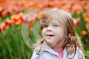 Cute curly hair blonde girl smiling with surprise on tulip bloss