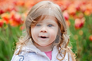 Cute curly hair blonde girl smiling with surprise on tulip bloss