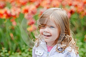 Cute curly hair blonde girl smiling with surprise on tulip bloss