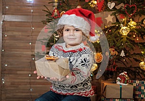 Cute curly-haired boy in a red Santa hat at the Christmas tree