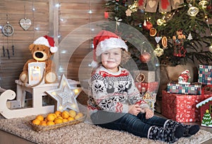 Cute curly-haired boy in a red Santa hat at the Christmas tree