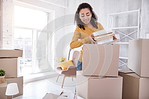 Cute curly-haired girl packing books before moving out