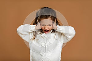 Cute curly little girl in white sweater is closing her ears