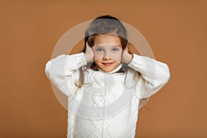 Cute curly little girl in white sweater is closing her ears