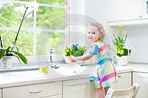 Cute curly toddler girl in colorful dress washing dishes