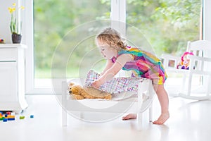 Cute curly toddler girl playing with her teddy bear