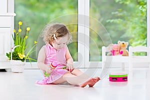 Cute curly toddler girl playing tambourine in a sunny white room