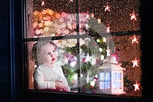 Cute curly toddler girl sitting with a toy bear at home during Christmas time, preparing to celebrate Xmas Eve