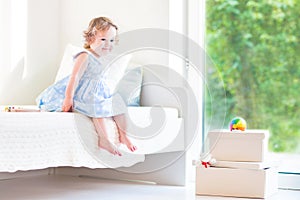 Cute curly toddler girl sitting on a white bed