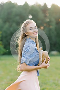 Cute cute girl student smiles dazzlingly and holds a hat in her hands on a summer walk