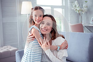 Cute dark-eyed daughter hugging her beaming caring mother